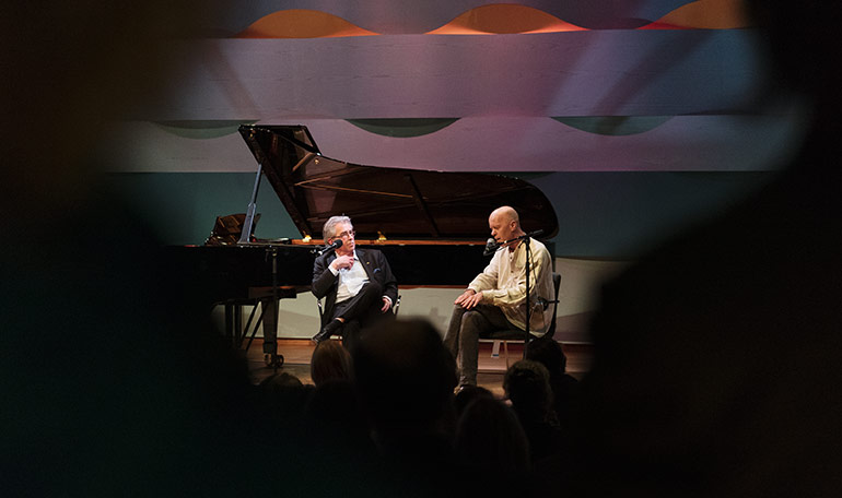 Två personer som samtalar på scenen i en konsertsal. Foto: Mira Åkerman