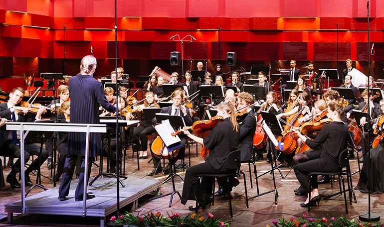 En symfoniorkester med dirigent i en konsertal.