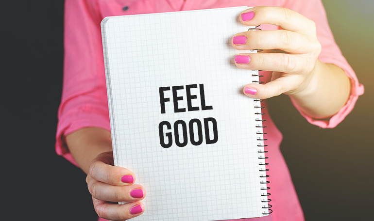 Kvinna med rosa tröja och naglar håller upp ett block med texten "feel good"